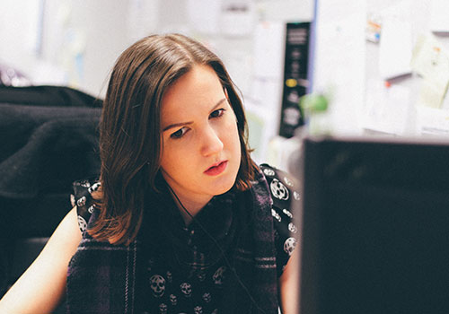A person who identifies as a female is sat at the the table looking at a screen.