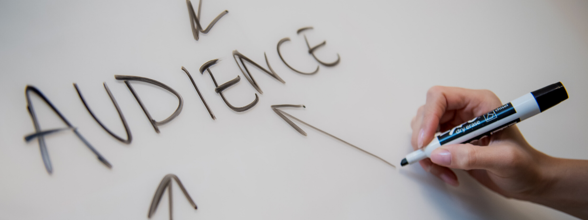 A hand writing the word ‘AUDIENCE’ on a whiteboard with arrows pointing towards it, symbolising audience targeting in SEO.