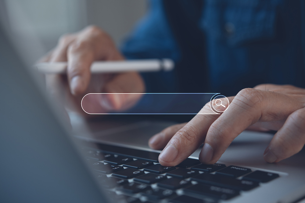 Close-up of a person typing on a laptop with a search bar overlay, representing search engine activity and SEO.