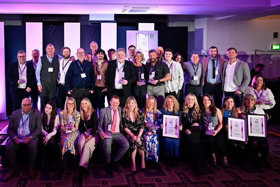 A large group of people posing at an awards event, with some holding trophies and framed certificates