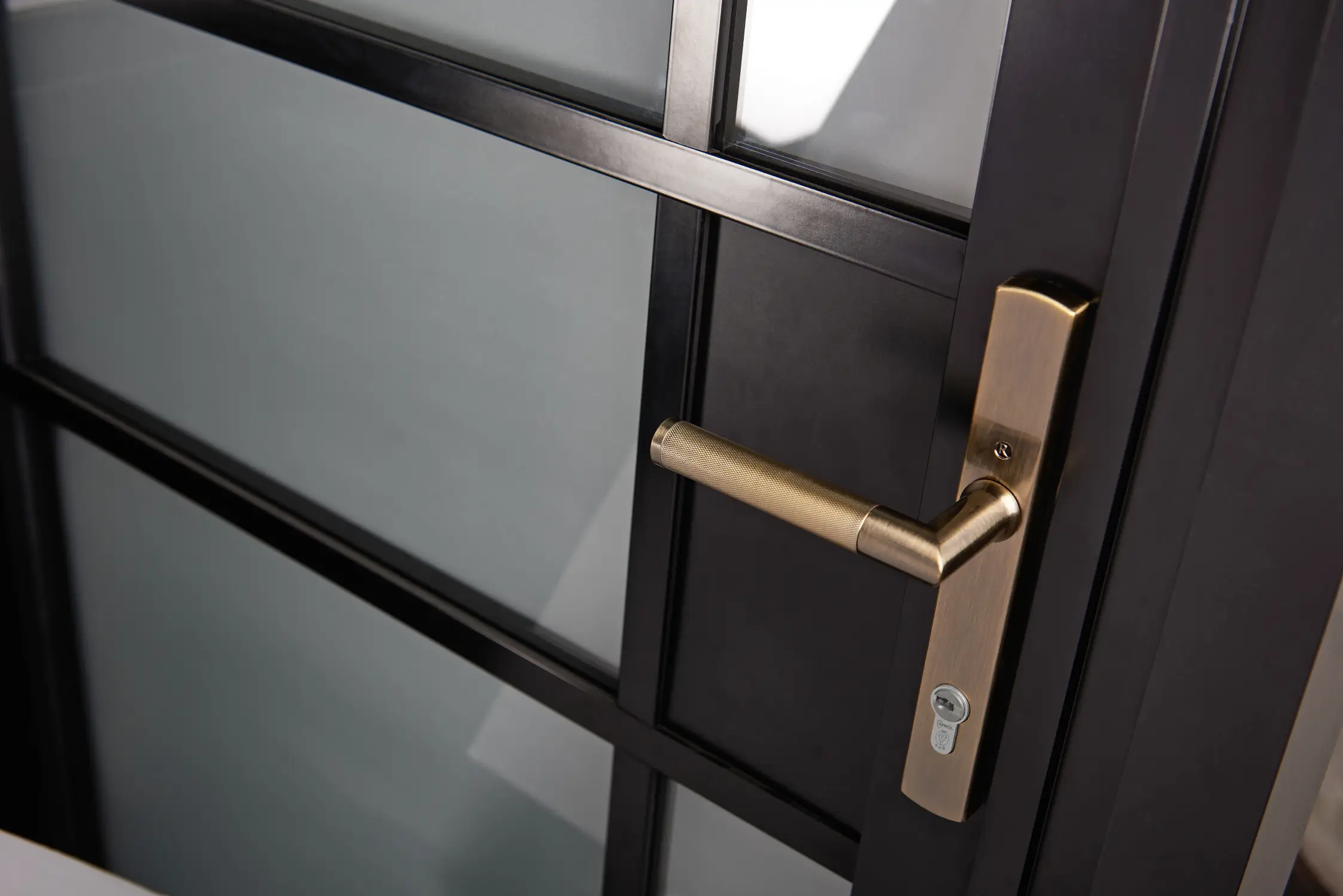Architectural hardware marketing image showing the WW19 knurled brass door handle installed on a modern metal framed glass door.